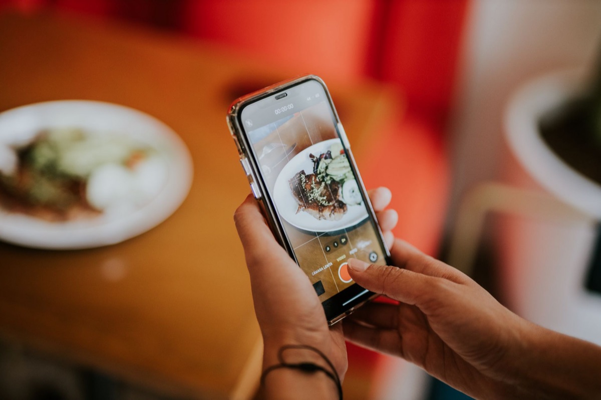 Un téléphone portable affichant une application de suivi des calories. L'écran est clair et lumineux, avec des chiffres et des graphiques. Le téléphone est posé sur une table en bois. L'ensemble est en lumière naturelle et douce.